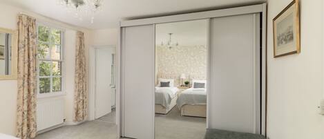 A bedroom with a large mirror, a bed, a bench, and a chandelier.