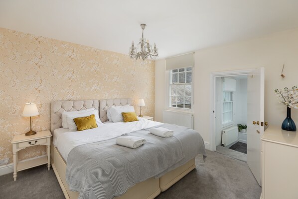 A bedroom with a large bed, bedside tables, a chandelier, and a view of a snowy landscape through a window.