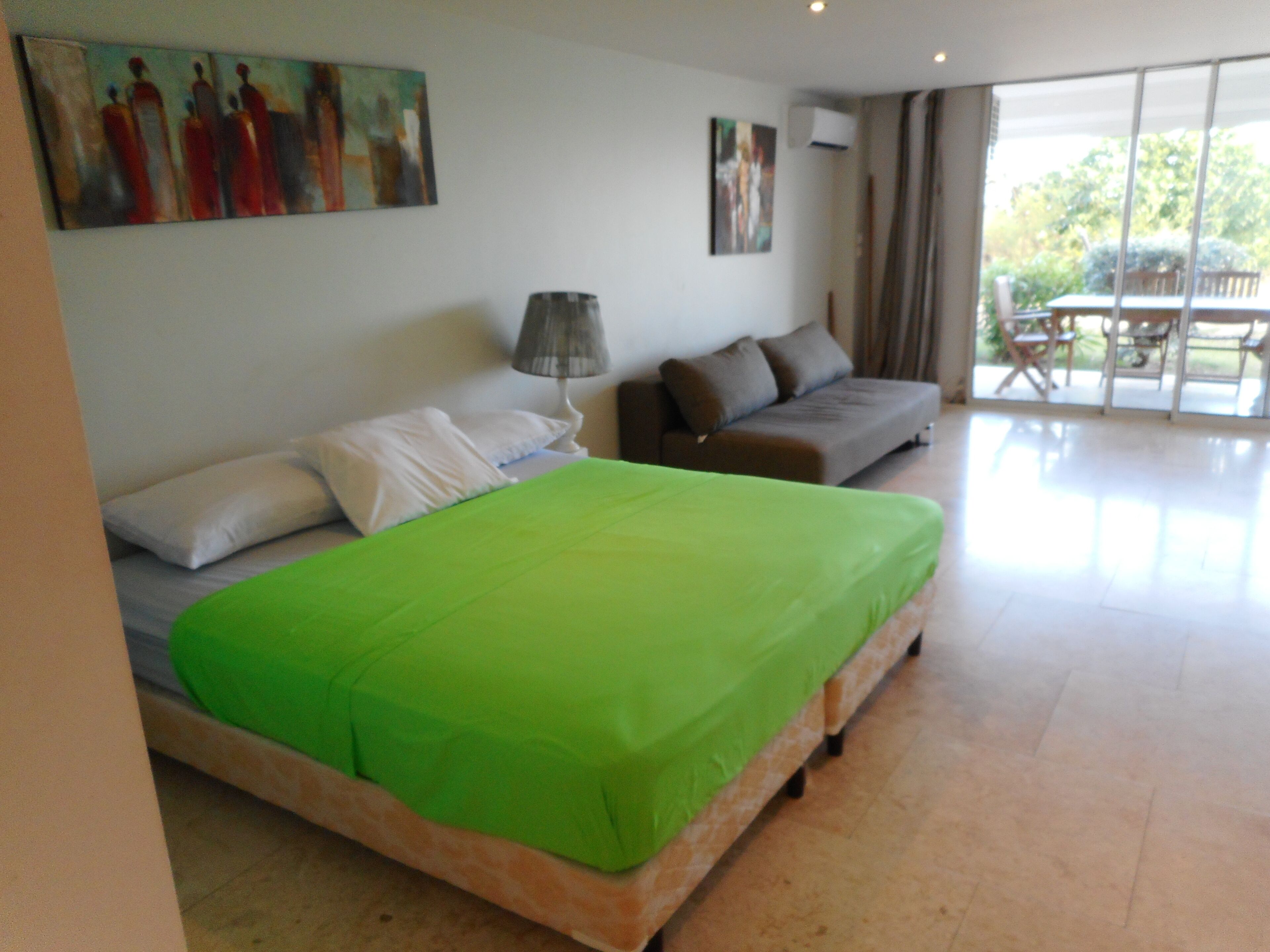 A bedroom with a bed, a sofa, a lamp, and a painting on the wall.