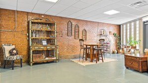 Una habitación con pared de ladrillo, una estantería de madera, una mesa con sillas y un ventanal grande.