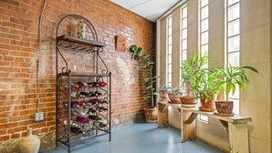 Una habitación con pared de ladrillo, botelleros, plantas en macetas y un banco de madera.