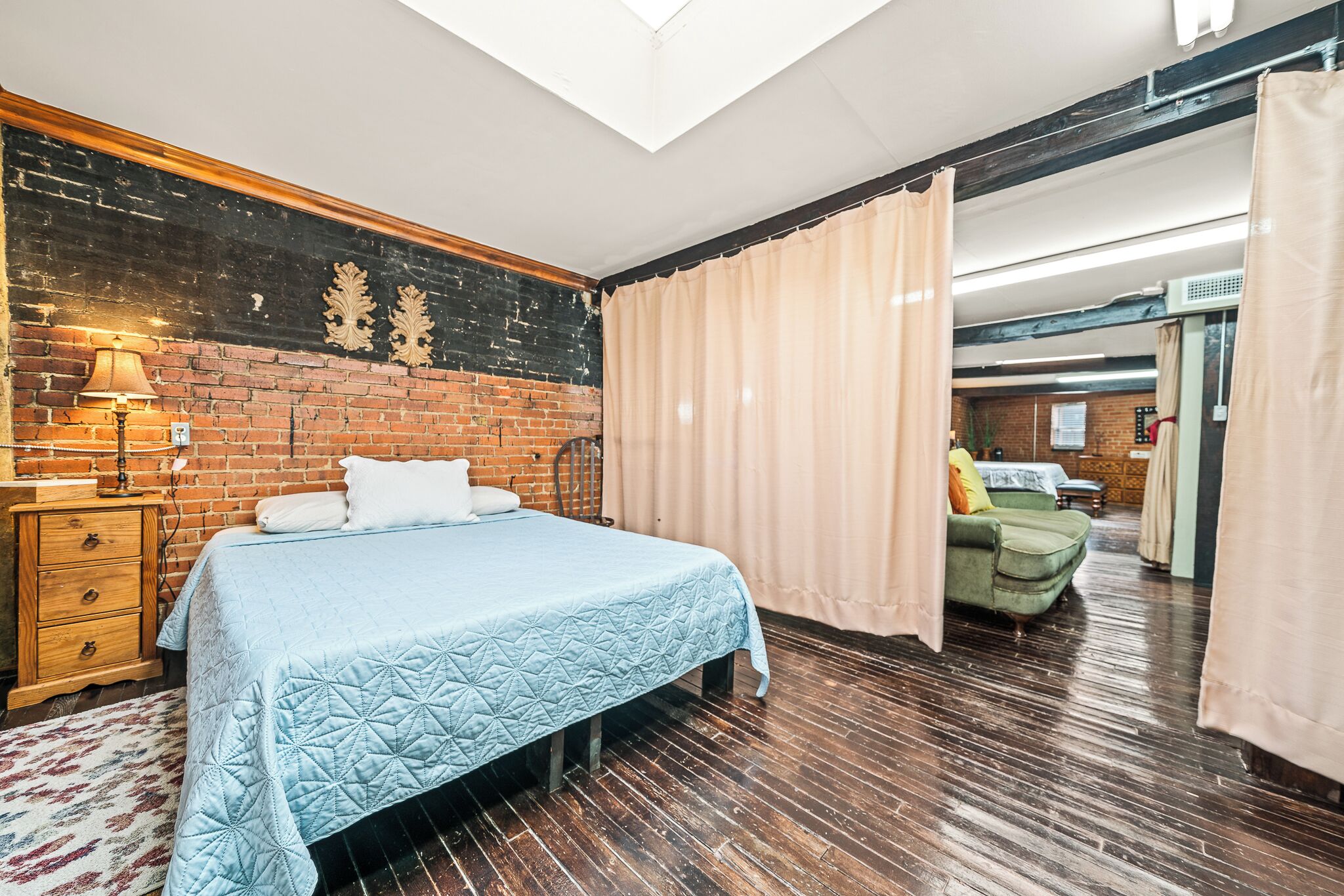 A room with a bed, wooden floor, brick wall, and a skylight.