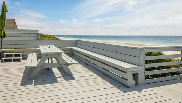 A wooden deck with a picnic table and benches overlooking a beach.