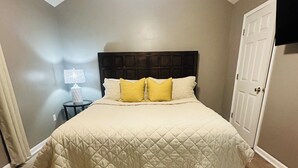 Un dormitorio con cama, mesita de noche, lámpara y puerta.
