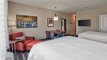 A hotel room with two beds, a desk with chairs, a TV, and artwork on the walls.