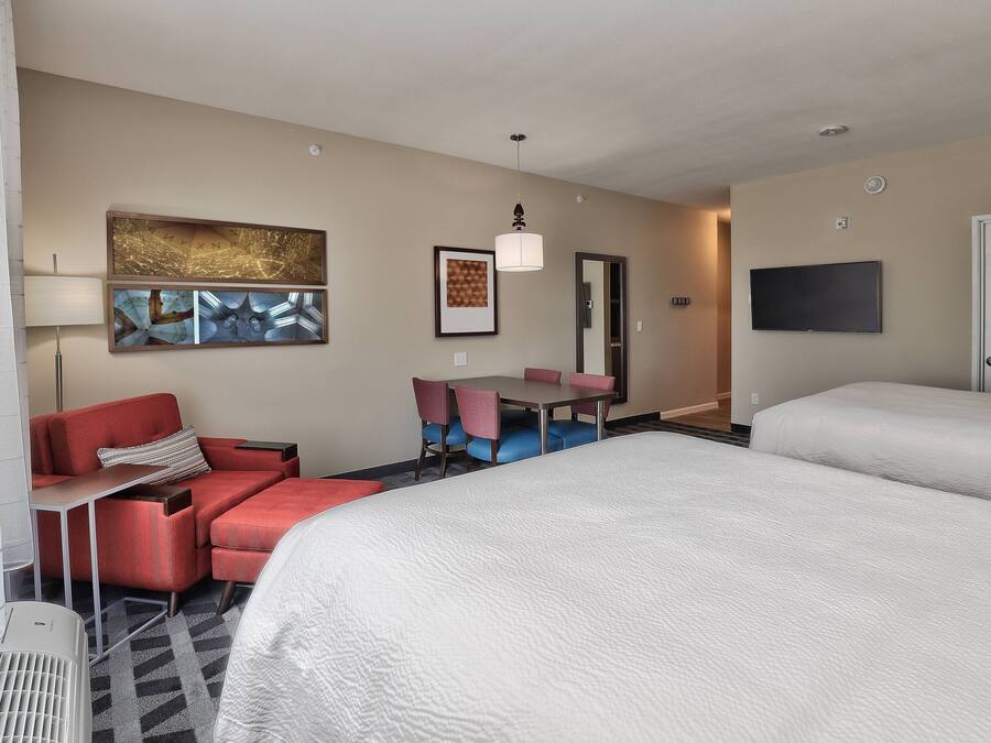 A hotel room with two beds, a desk with chairs, a TV, and artwork on the walls.