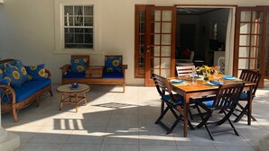 Eine sonnendurchflutete Terrasse mit einem Holztisch, Stühlen, einer blauen Couch und einem kleinen runden Tisch mit einer Schüssel.