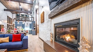 Una sala moderna con chimenea, un sofá y una cocina al fondo.