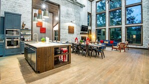 Una cocina amplia con una isla central, un área de comedor con sofá y grandes ventanales con vistas a árboles.