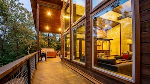 Una terraza de madera con zona de estar y amplios ventanales con vistas a un bosque.
