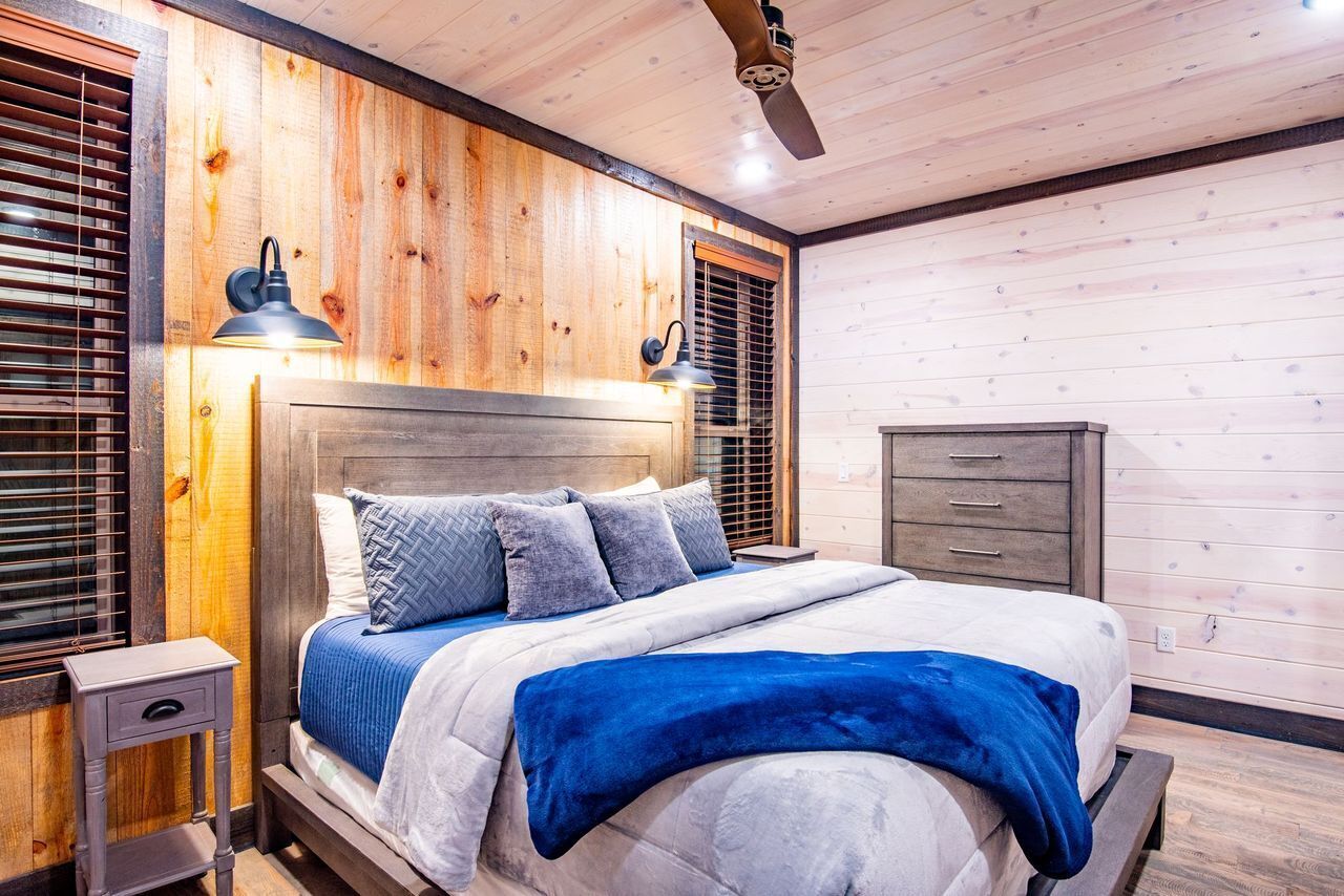 Une chambre à coucher avec une tête de lit en bois, un lit recouvert d’une couette bleue et blanche, deux lampes de chevet et une table de chevet en bois.