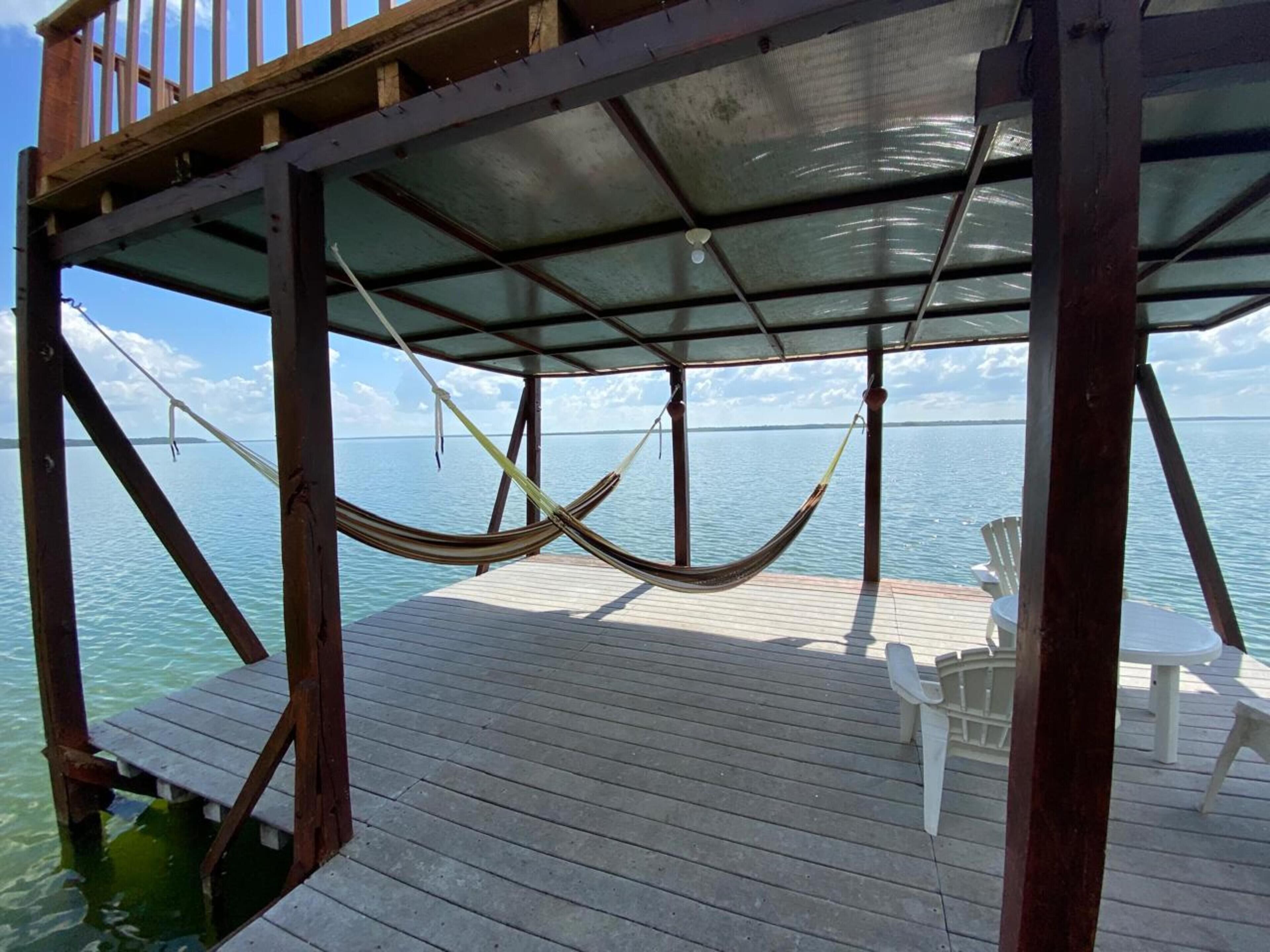 A wooden deck with a hammock and a chair, overlooking a calm sea.