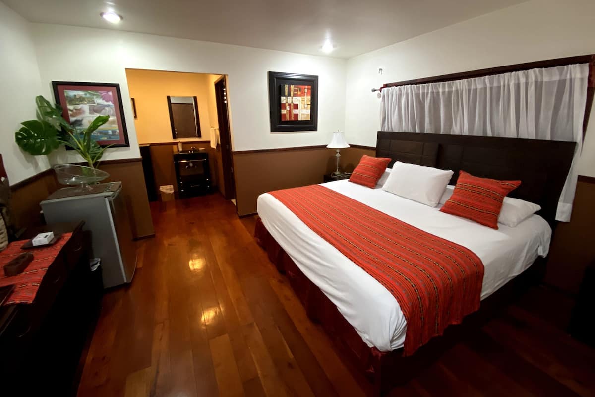 Une chambre d’hôtel avec un grand lit, un bureau, un miroir et une plante.
