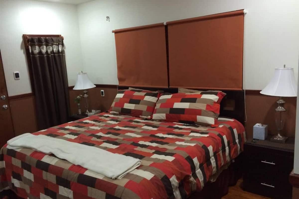 Un lit avec une couvre-lit à carreaux, une table de chevet avec une lampe et une fenêtre avec des rideaux.