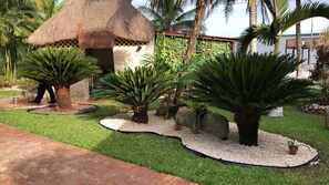 Un jardín tropical con palmeras, una estructura de techo de paja y un sendero.