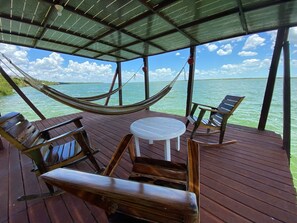 A wooden deck with a hammock, wooden chairs, and a small round table. - Coras Place Bacalar Lagoon Front (Bacalar)