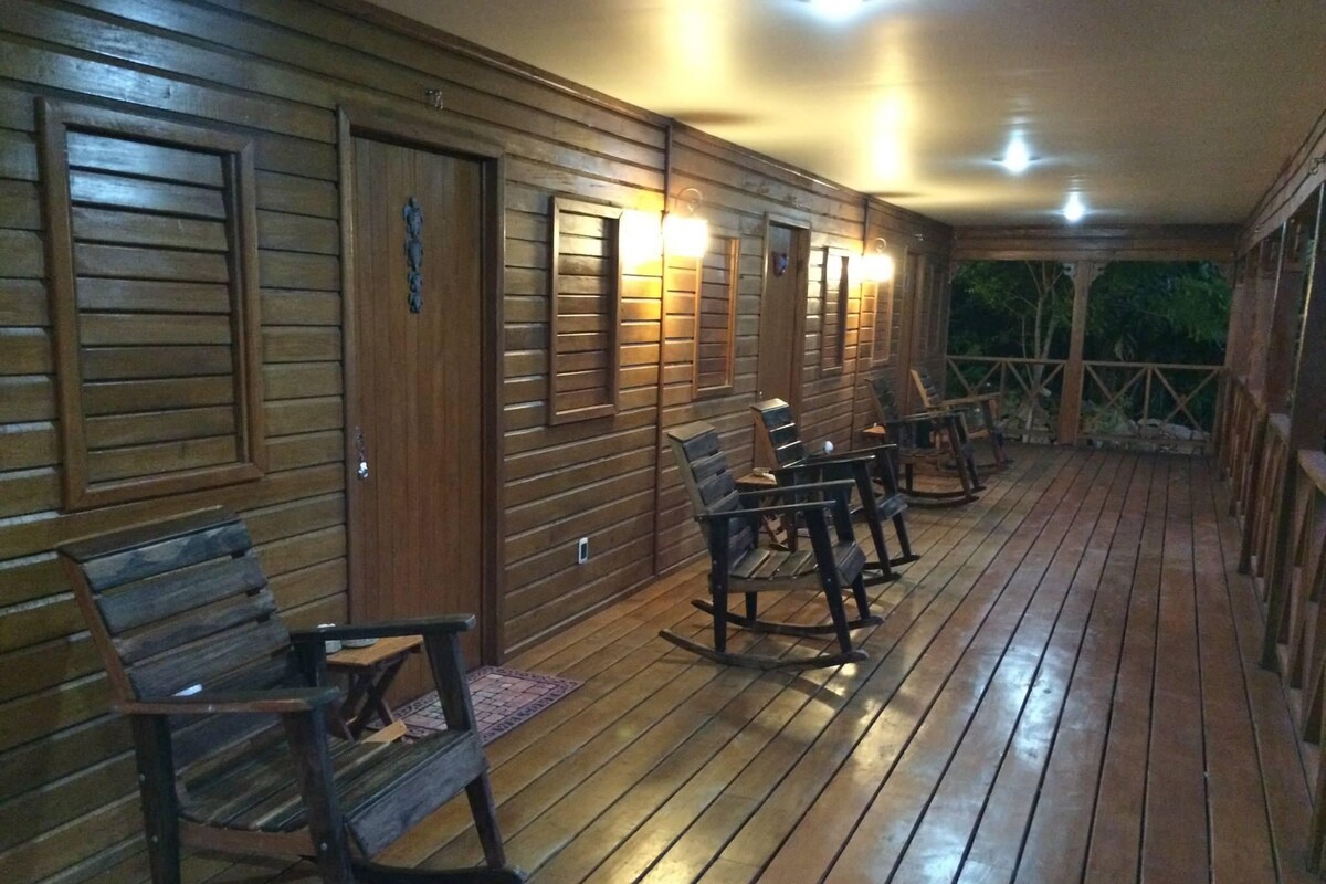 A wooden deck with rocking chairs and a covered area with wall-mounted lights.