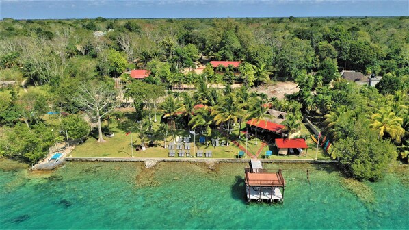 Vista aérea de un resort tropical con aguas turquesas cristalinas, un muelle y varios edificios con techos rojos.