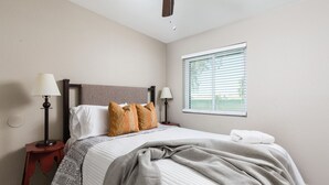 A neatly made bed with patterned bedding, two bedside lamps, and a window with blinds. - The Diamond - Private Pool / Pet Friendly / 4BD Near Arena (Phoenix)