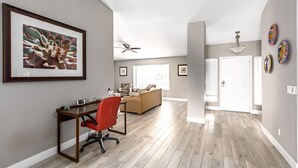 A spacious living area with a wooden floor, a red office chair, a beige sofa, and a ceiling fan. - The Diamond - Private Pool / Pet Friendly / 4BD Near Arena (Phoenix)