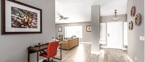 Un vaste espace de vie doté d’un plancher en bois, d’un fauteuil de bureau rouge, d’un canapé beige et d’un ventilateur de plafond.