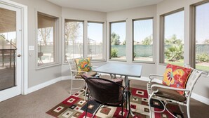 A sunroom with a table and chairs, large windows, and a view of the backyard. - The Diamond - Private Pool / Pet Friendly / 4BD Near Arena (Phoenix)