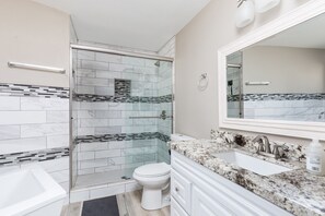 A modern bathroom with a glass-enclosed shower, a white toilet, a sink with a marble countertop, and a large mirror above the sink.