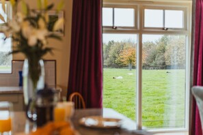 A dining area with a table, chairs, and a window overlooking a grassy field with trees. - Cart House 4 bedrooms - sleeps 9 guests  in 4 bedrooms (Beverley)