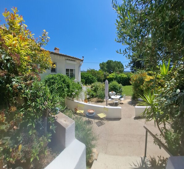 Eine Terrasse mit Gartenmöbeln, ein weißes Gebäude und üppiges Grün.