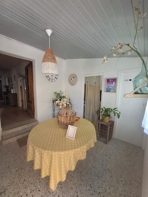 Ein Zimmer mit einem runden Tisch, der mit einer gemusterten Tischdecke bedeckt ist, einer hängenden Holzleuchte, einer Uhr und einem Blumentopf.
