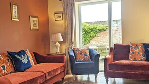 A cozy living room with two sofas, a lamp, and a view of a brick wall and greenery outside. - Barn House, Broadgate Farm Cottages - sl 8 in 4 bedrooms (Beverley)