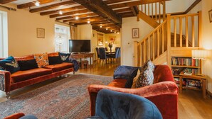 A cozy living room with a red sofa, blue armchair, and a wooden staircase. - Barn House, Broadgate Farm Cottages - sl 8 in 4 bedrooms (Beverley)
