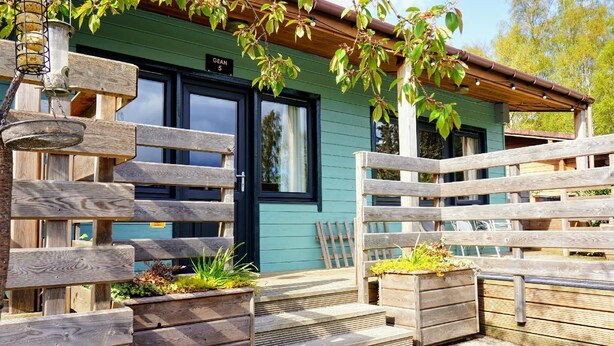 A wooden fence with a bench and planter boxes in front of a building with a green exterior and a black door.