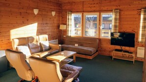 L’intérieur d’un chalet accueillant, avec un canapé en cuir, une petite table, un téléviseur et une fenêtre avec des rideaux.