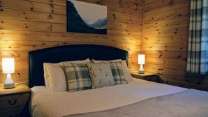 Habitación con paneles de madera, una cama, dos lámparas de noche y un cuadro en la pared.