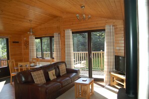 L’intérieur d’un chalet en bois, avec un canapé en cuir, un téléviseur et un balcon doté d’une balustrade en bois.