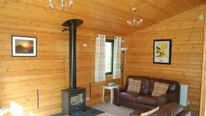 A cozy cabin interior with a wooden interior, a sofa, a table, a lamp, and a fireplace.