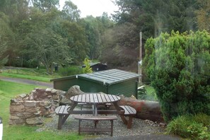 Escape to a serene natural setting surrounded by trees and shrubs, with a charming picnic area featuring a wooden table and benches.
