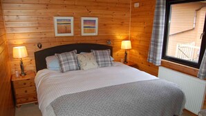 Ein Schlafzimmer mit Holzvertäfelung, einem Bett, zwei Nachttischlampen und zwei gerahmten Bildern an der Wand.