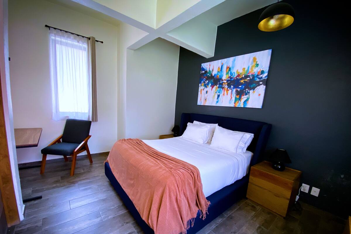 A modern bedroom with a large bed, a chair, a nightstand, and a painting on the wall.