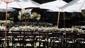Tische im Freien mit weißen Sonnenschirmen und floralen Tischdekorationen.