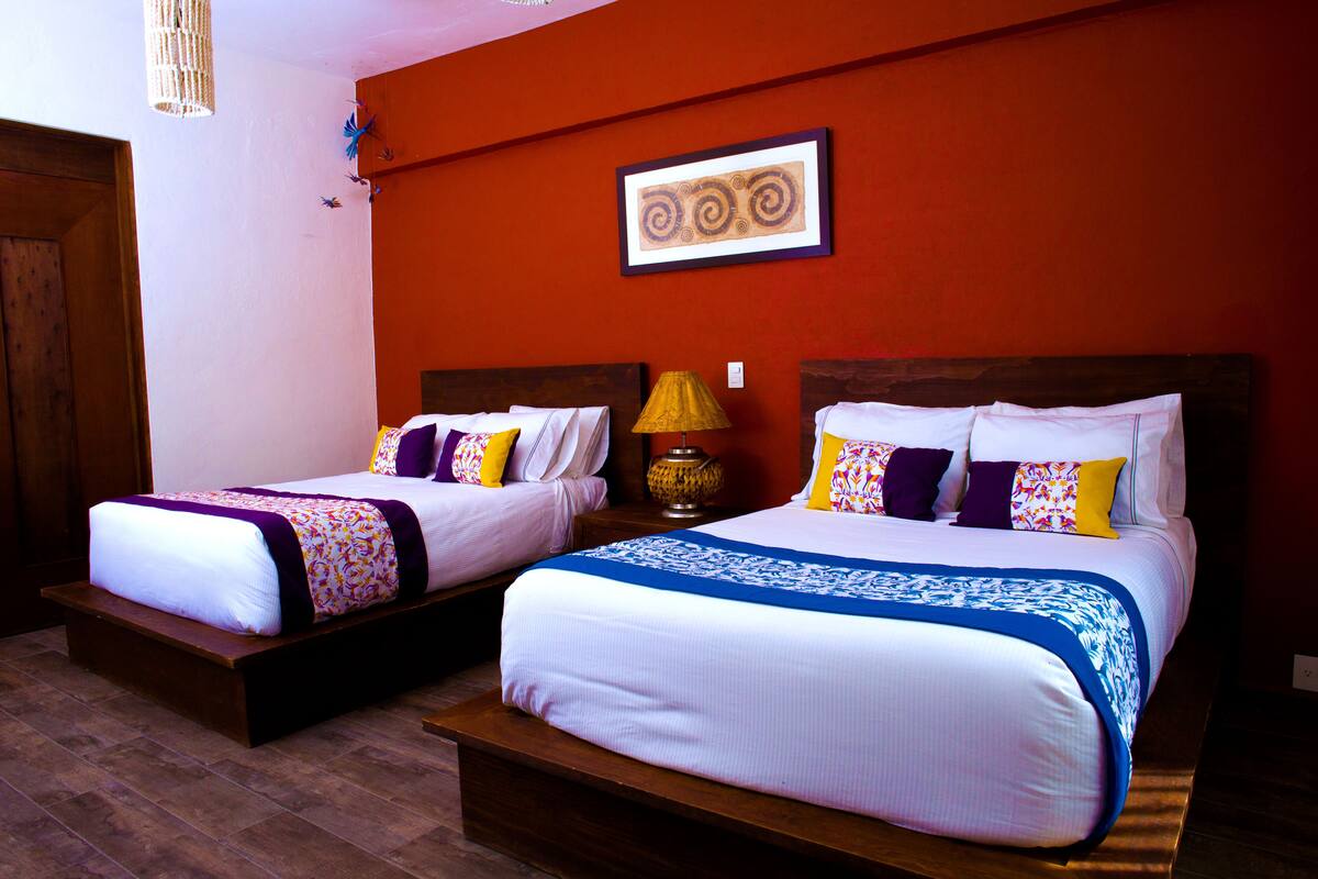 Two double beds with wooden headboards, a wall-mounted artwork, and a floor lamp.
