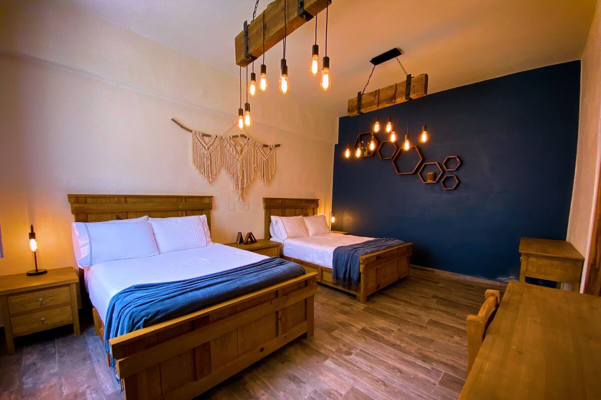 A double bed with a wooden headboard, a bedside table with a lamp, and a wall-mounted macrame decoration.
