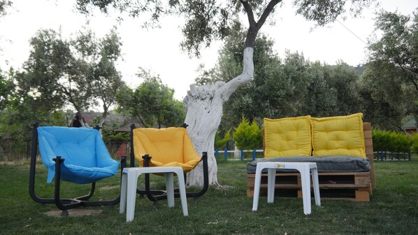 Two outdoor seating areas with chairs and tables, surrounded by trees and grass. - Concept Bungalow (Ayvacik)