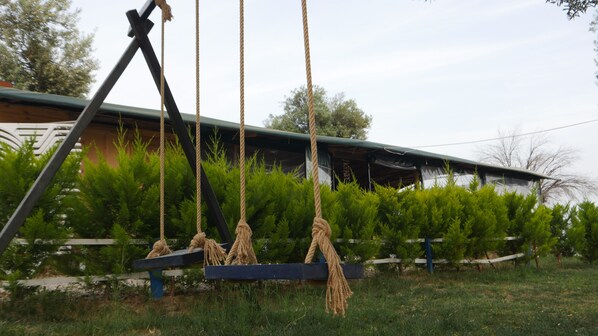 A swing set with ropes and a wooden bench in front of a building with a slanted roof. - Concept Bungalow (Ayvacik)