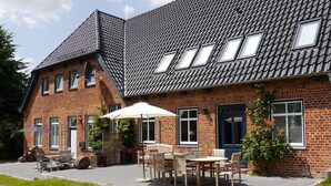 Une maison en briques avec un toit en pente, de nombreuses fenêtres et un patio aménagé avec du mobilier d’extérieur.