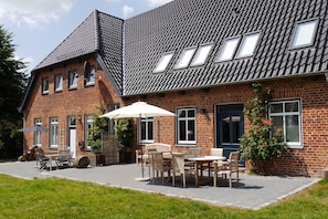 Een huis van baksteen met een schuin dak, meerdere ramen en een terras met tuinmeubilair.
