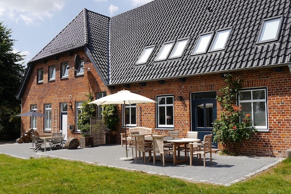A brick house with a sloped roof, multiple windows, and a patio area with outdoor furniture.