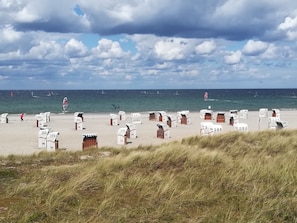 A beach with numbered beach huts and a view of the sea with sailboats.