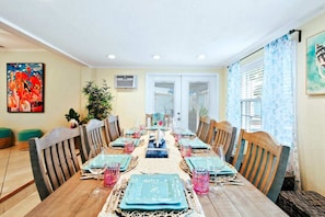 A dining area with a long wooden table set for six, surrounded by wooden chairs.